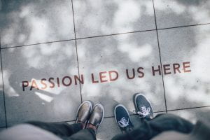 Text on ground "passion led us here" with two sets of people's feet visible as if looking down on text